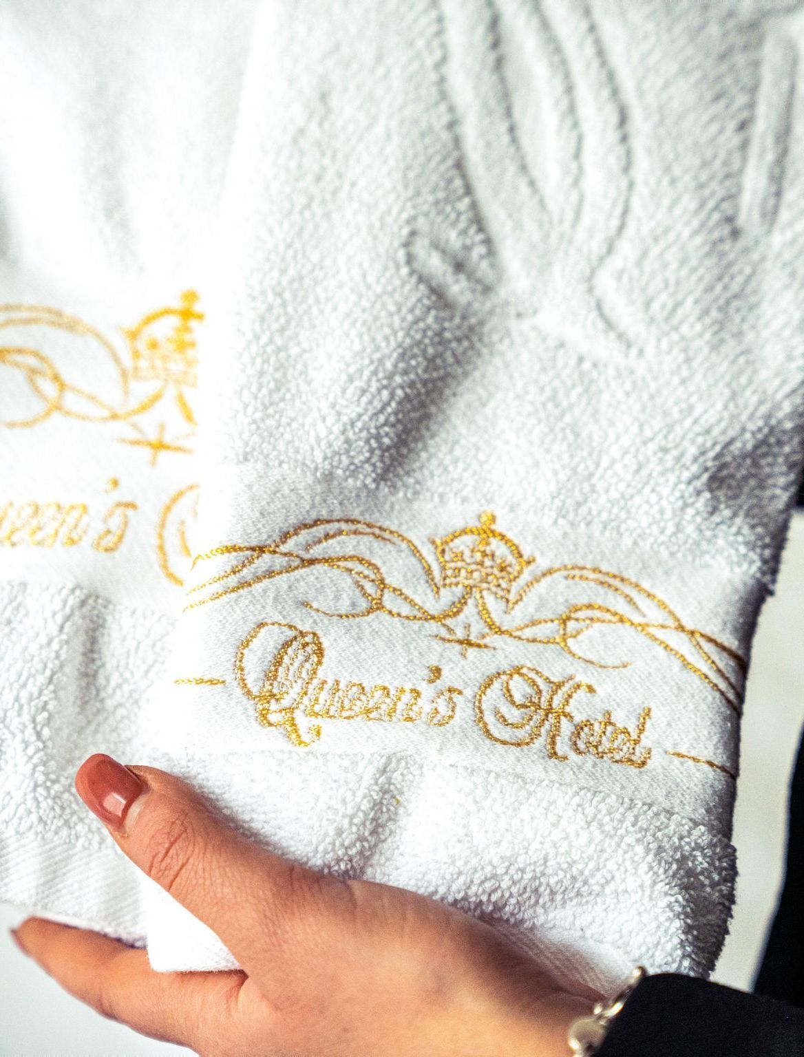 White towel with gold embroidered “Queen’s Hall” logo, held by a hand.