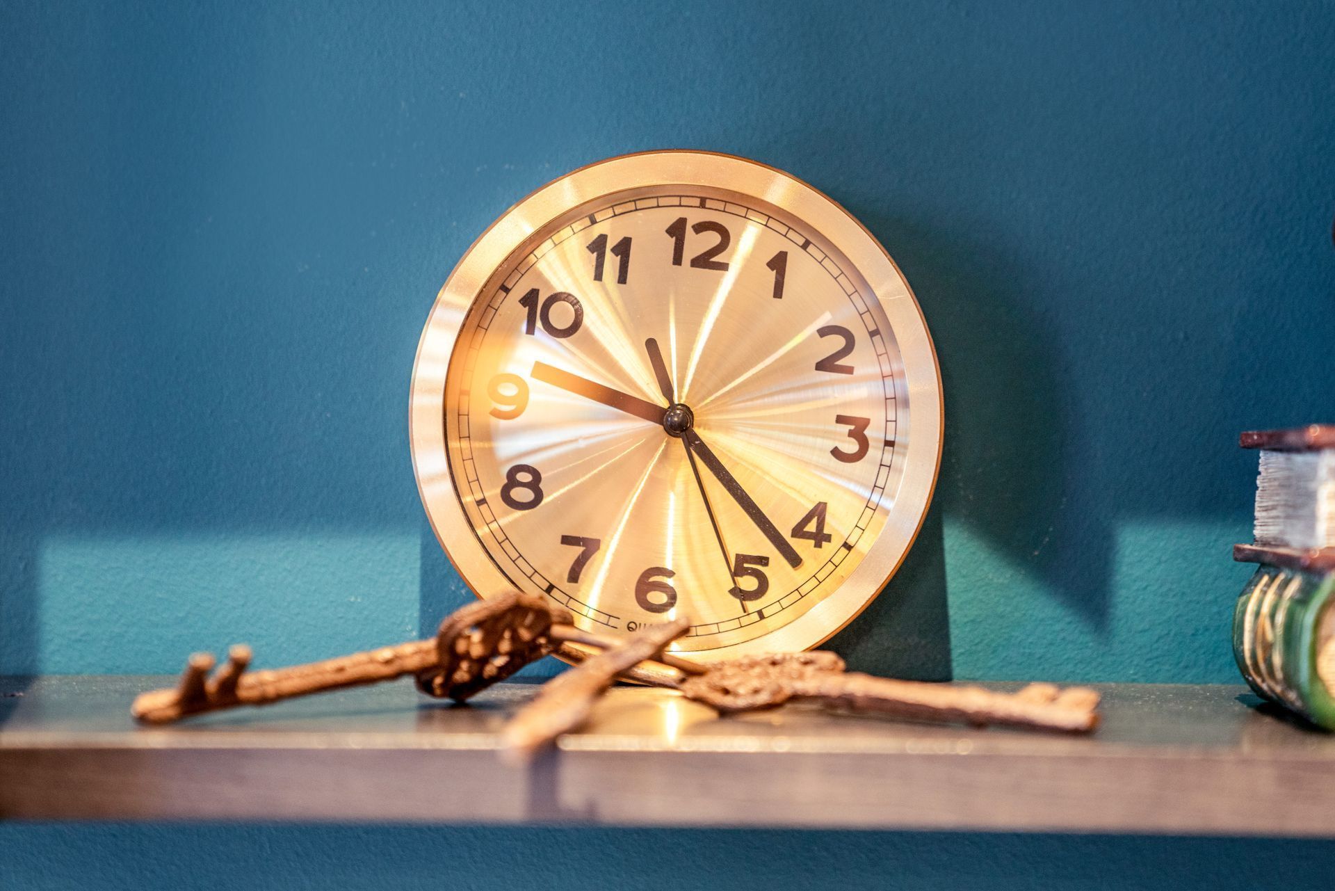 Wooden clock with Roman numerals on a blue tabletop, with books at the right edge