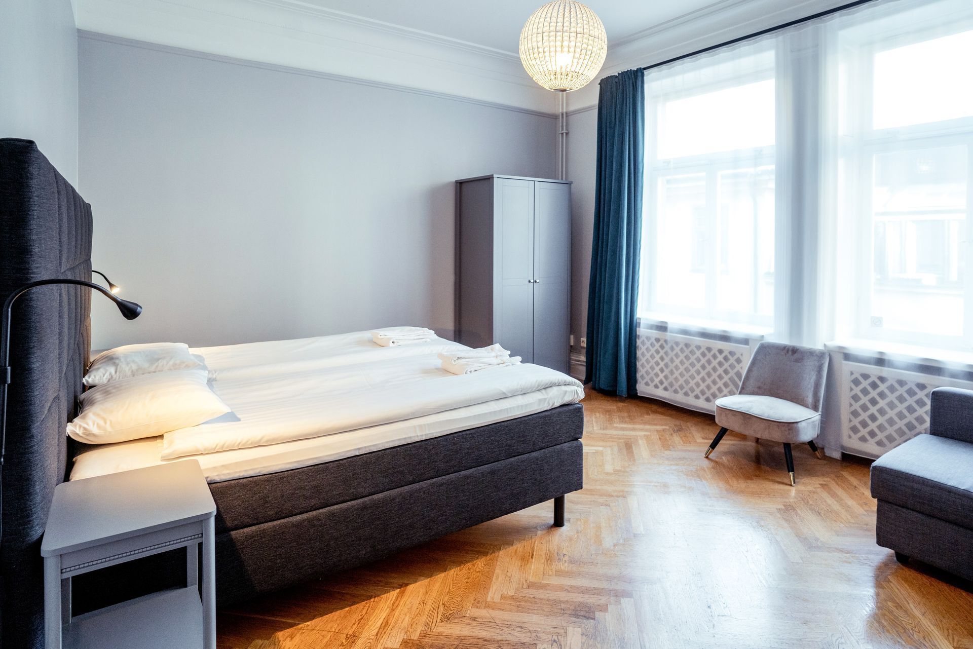 Modern bedroom with made bed, large windows, gray walls, and wooden floor