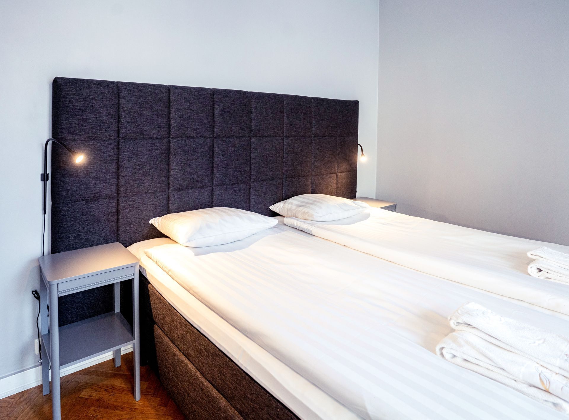 Small bedroom with two neatly made twin beds, gray headboards, and a bedside table.