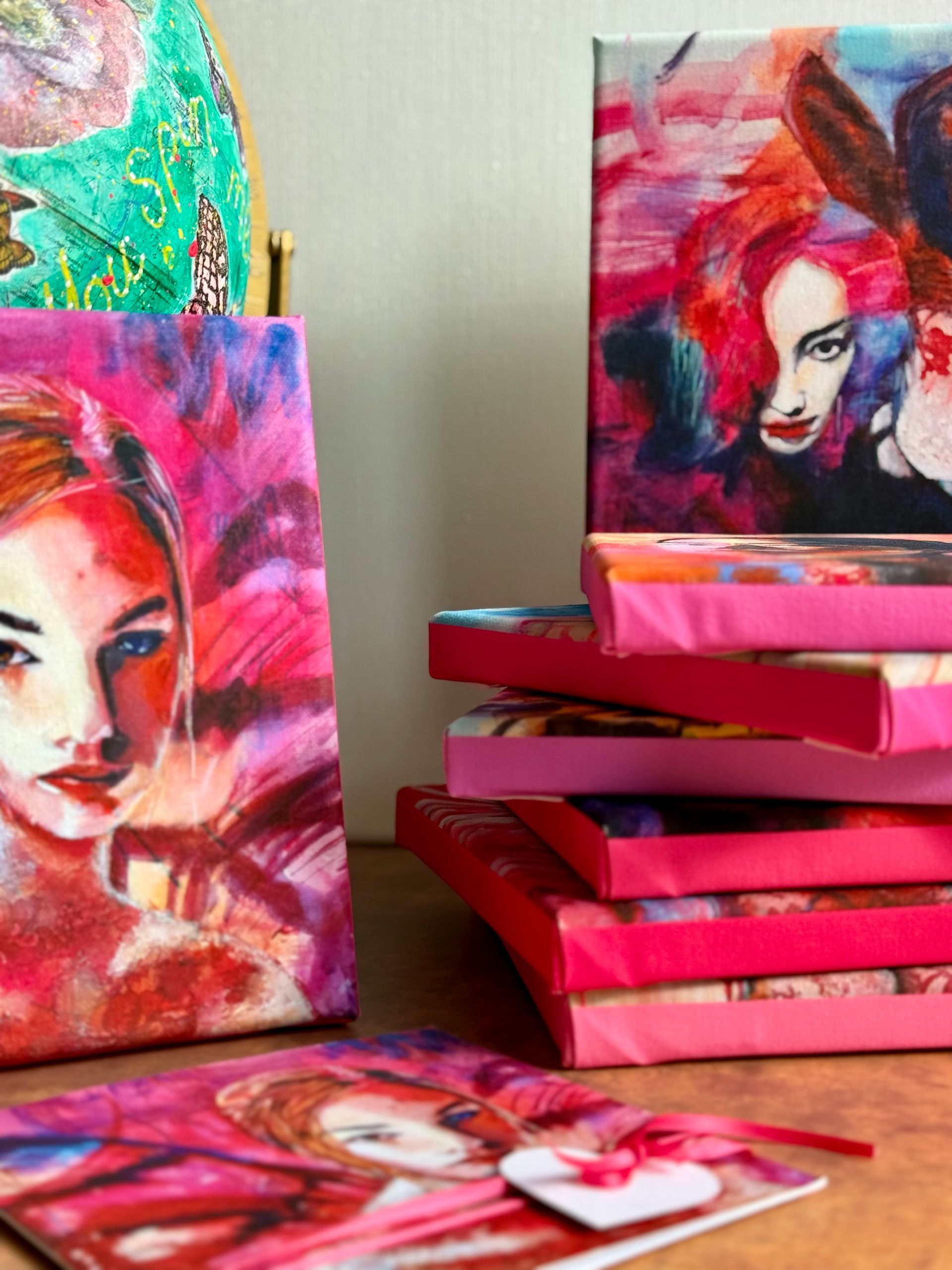 Paintings of women in pink hues, stacked with a greeting card in front.