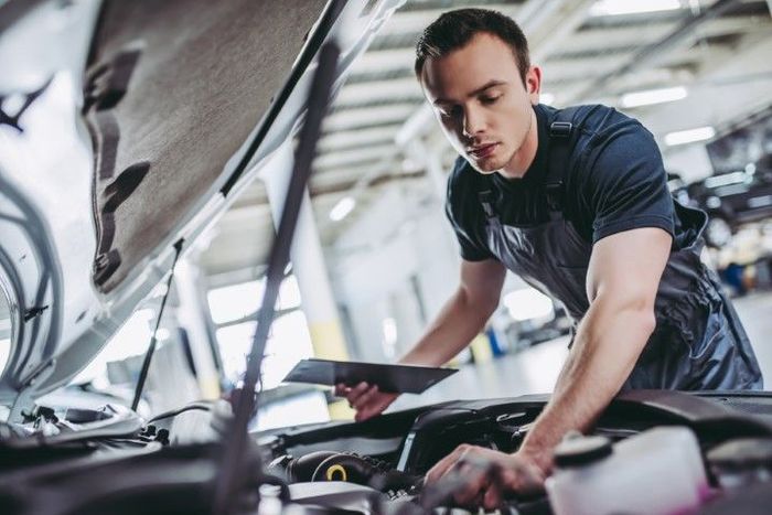 Mechanic inspecting car engine with tablet in auto repair shop.