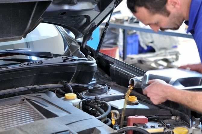 Mechanic pouring oil into a car engine with the hood open.