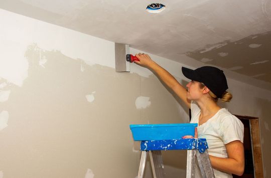 Drywall contractor applying mudding compound to walls and ceiling