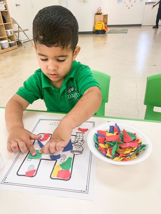 A young boy in a green shirt is sitting at a table playing with a bowl of stickers.