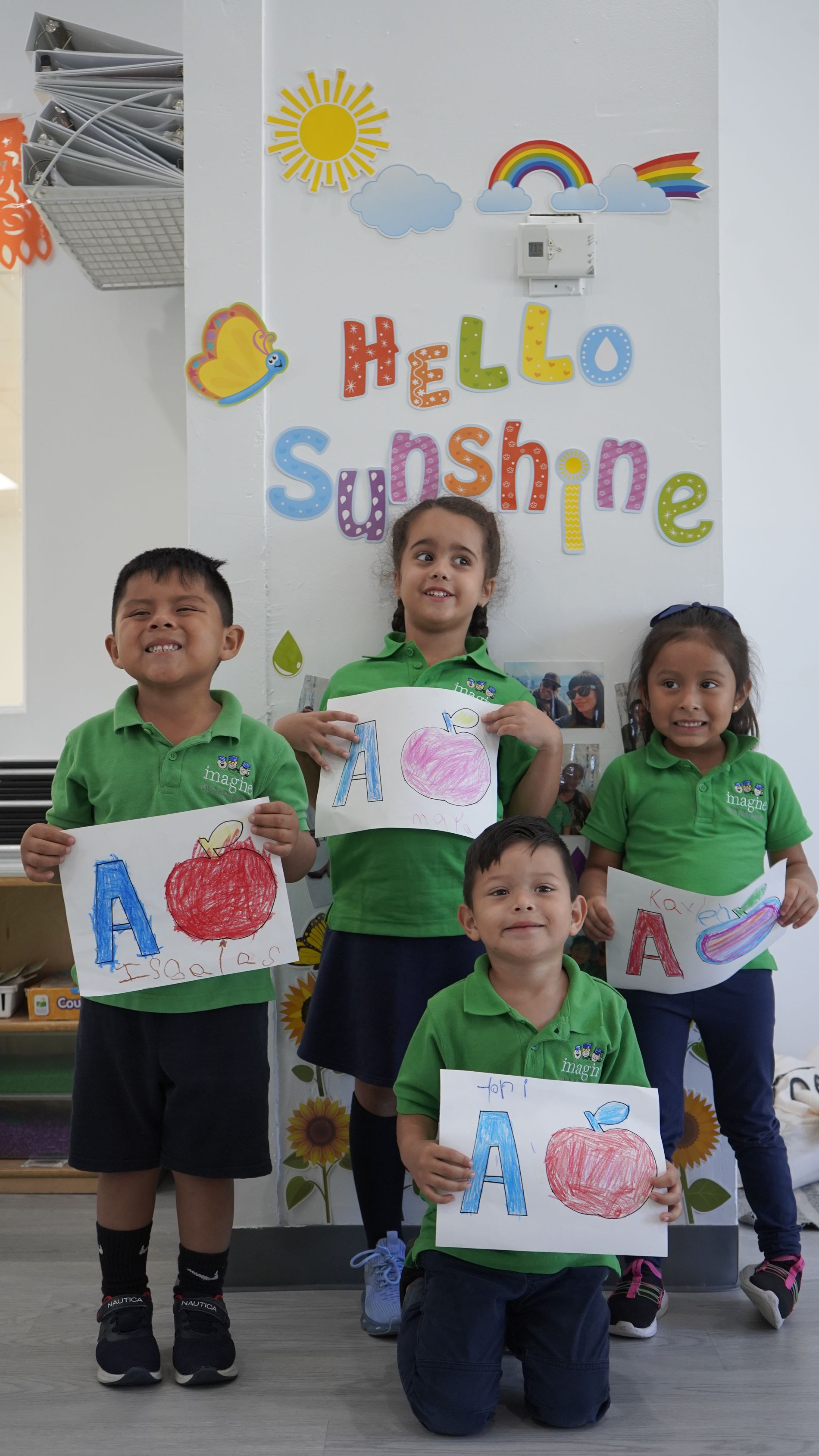A group of children are posing for a picture in front of a wall that says hello sunshine.