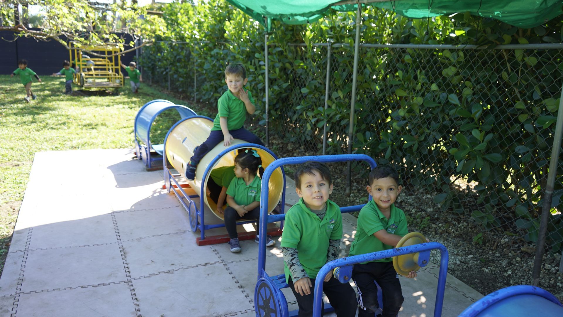 A group of children in green shirts are riding a toy train