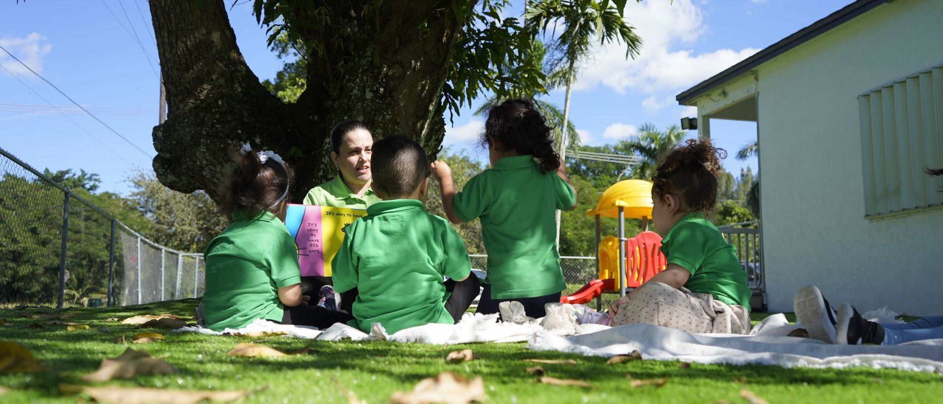 A group of children are sitting under a tree on a blanket.