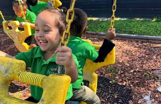 A group of children are sitting on yellow swings at a playground.