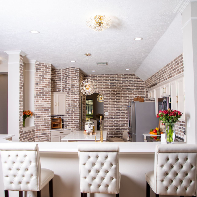 Bright kitchen with white cabinets, marble countertops, and rattan bar stools.