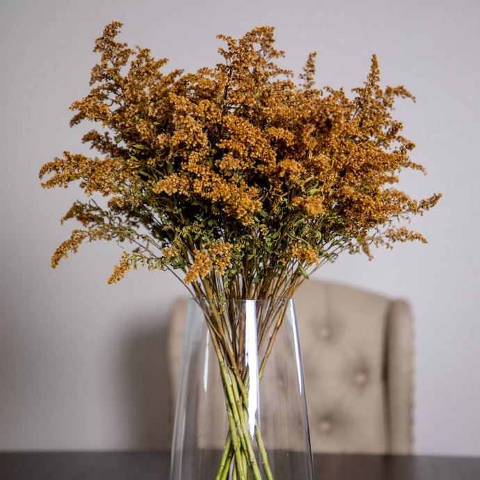 White kitchen with island, seating, pendant lights, and a view of green trees through a window.