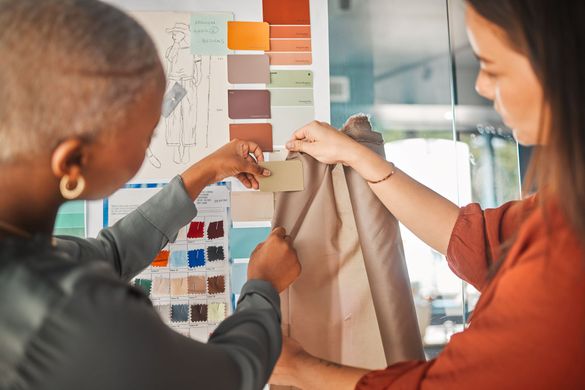 Two women choosing fabric samples with color swatches in a design studio.