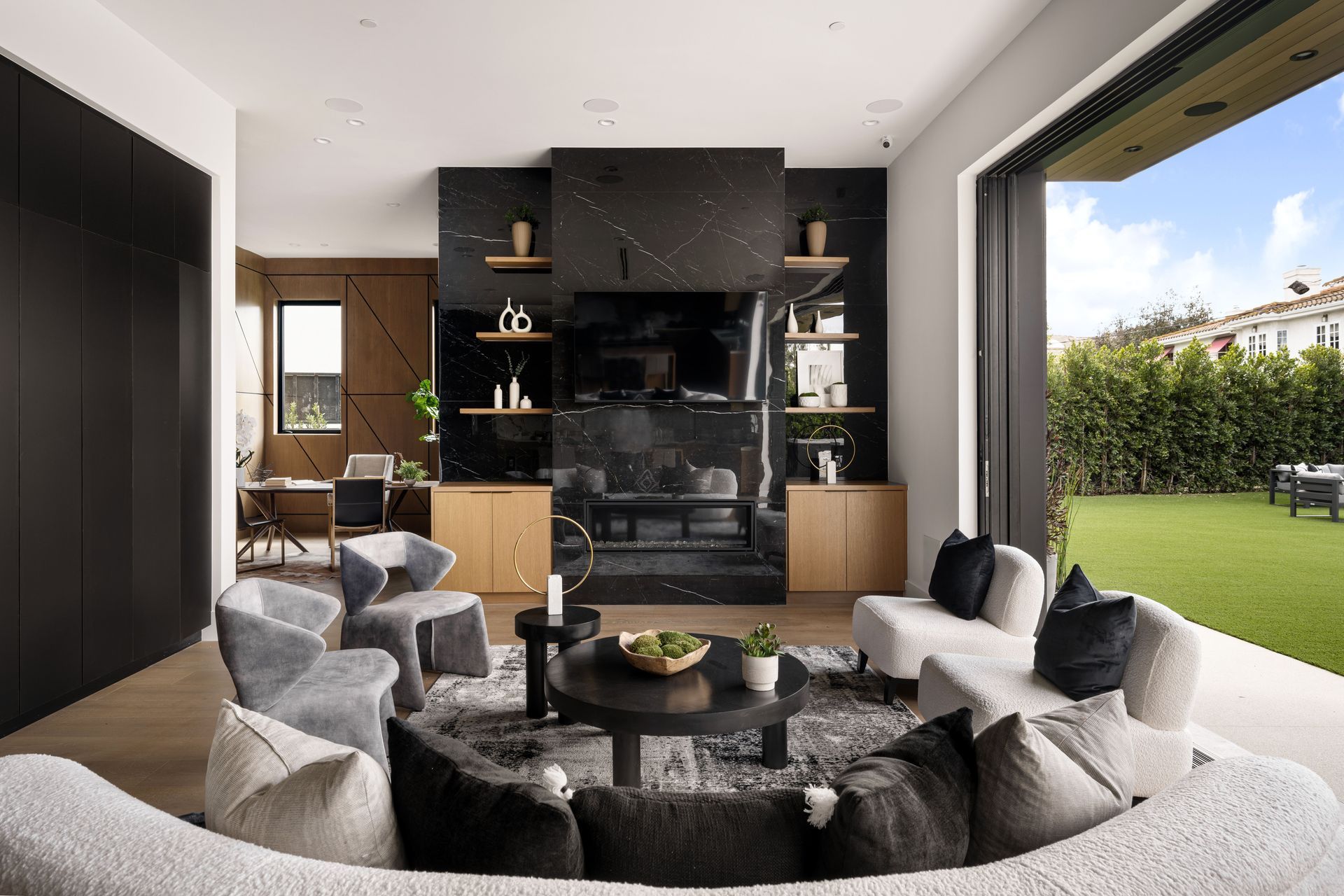 Modern living room with black marble fireplace, seating area, and open to a grassy backyard.