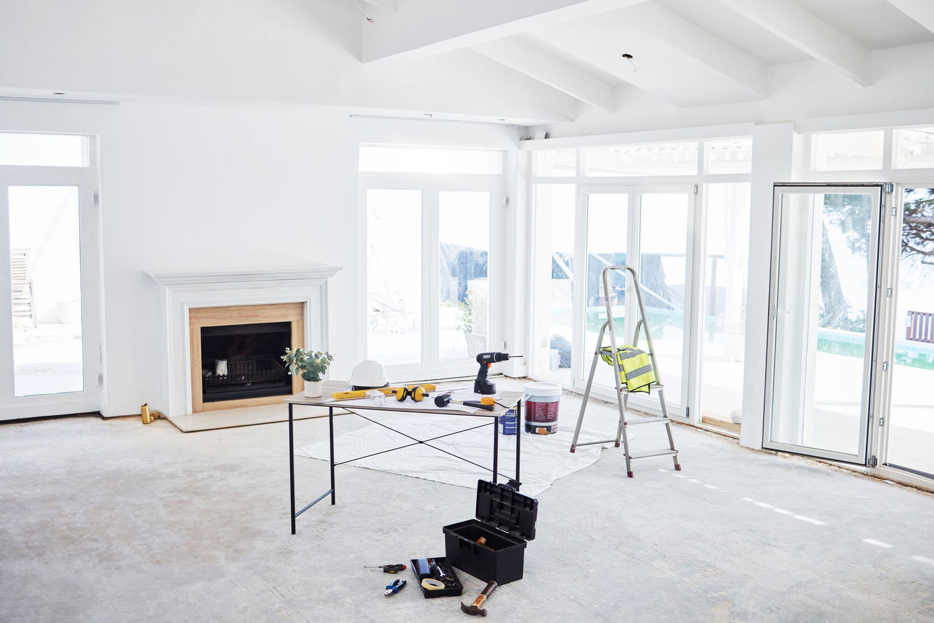 Renovated interior. White room with fireplace, table with tools, ladder, and large windows.