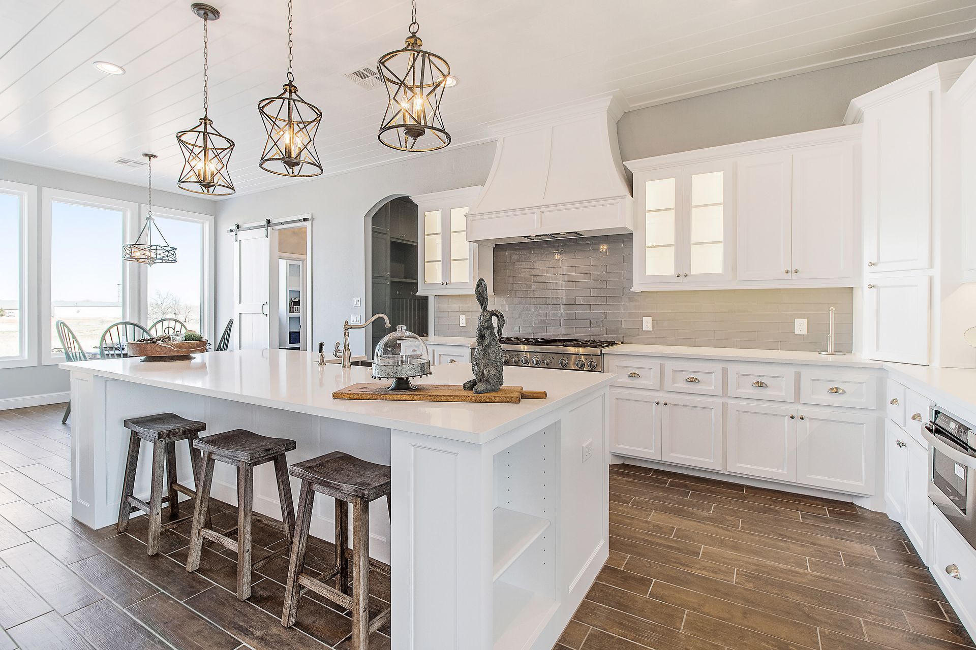 Spacious white kitchen with island, wooden stools, hanging lights, and hardwood floors.