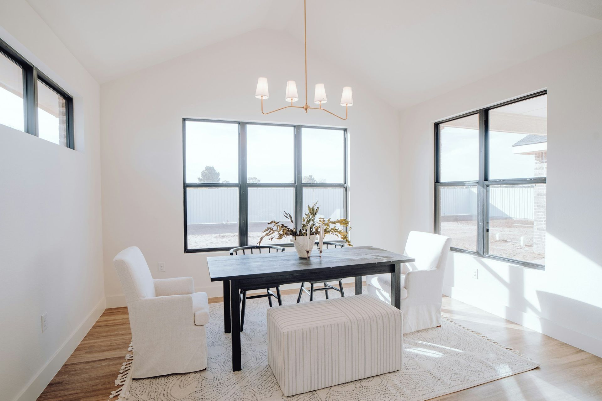 Bright dining room with a black table, white chairs, and large windows.