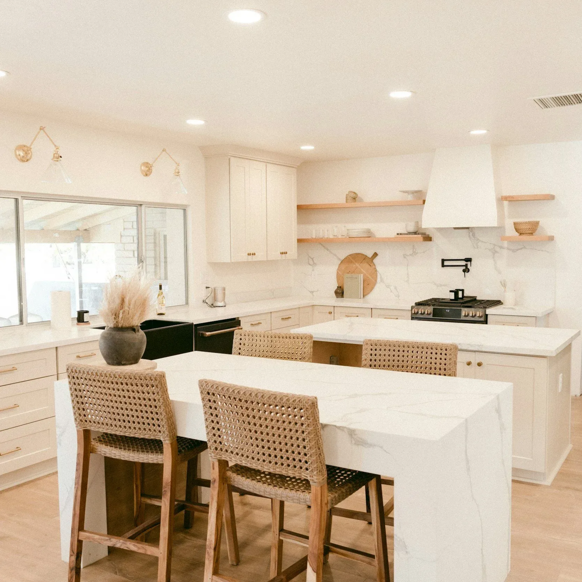 Bright kitchen with white cabinets, marble countertops, and rattan bar stools.