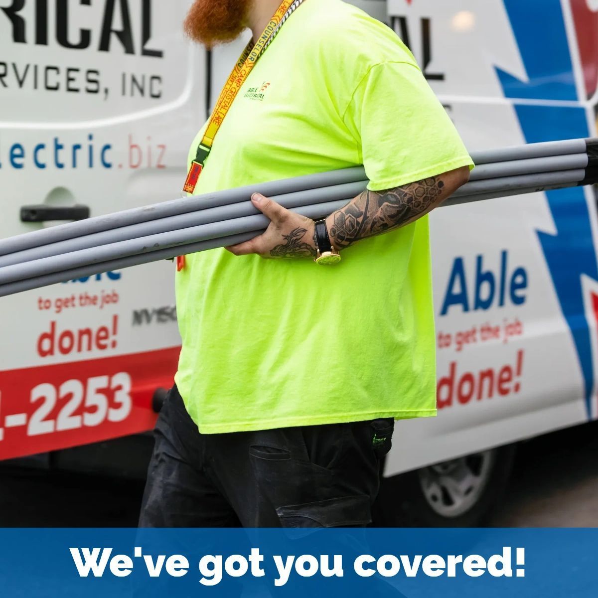 A person wearing a neon yellow shirt carries grey conduit pipes in front of a service van with 