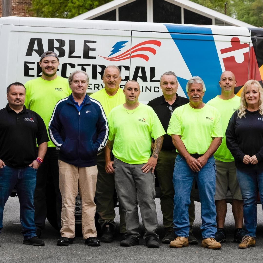 A group of nine people in work attire standing in front of an Able Electrical Services van.
