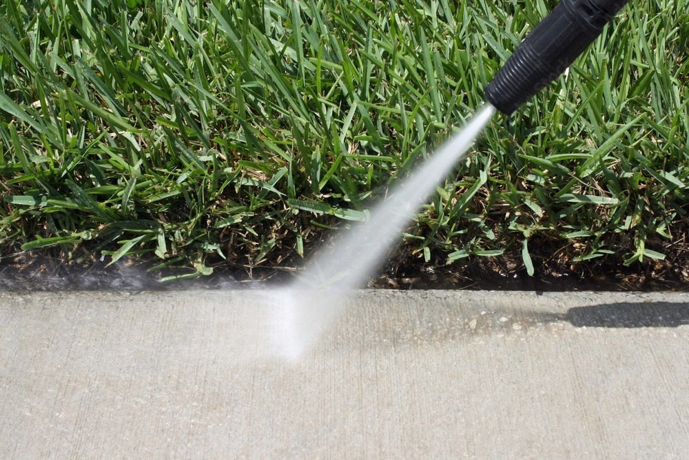 A person is using a high pressure washer to clean a sidewalk.