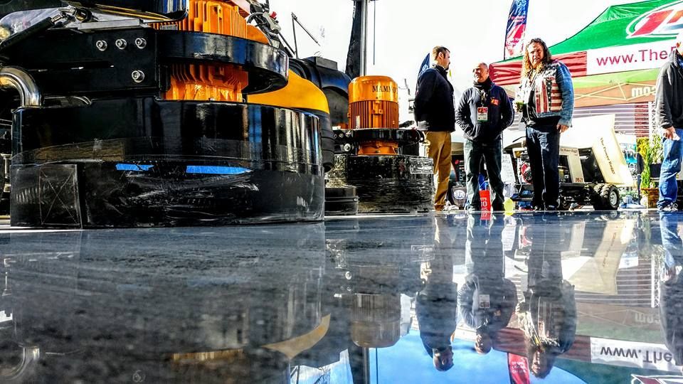Shiny floor reflecting people at an outdoor event. Machinery with yellow lights.