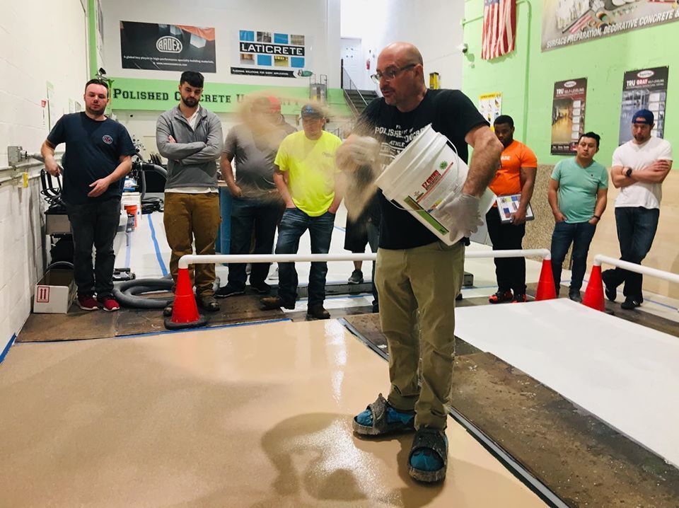 Man pouring material on a floor during a training session; several people observe.