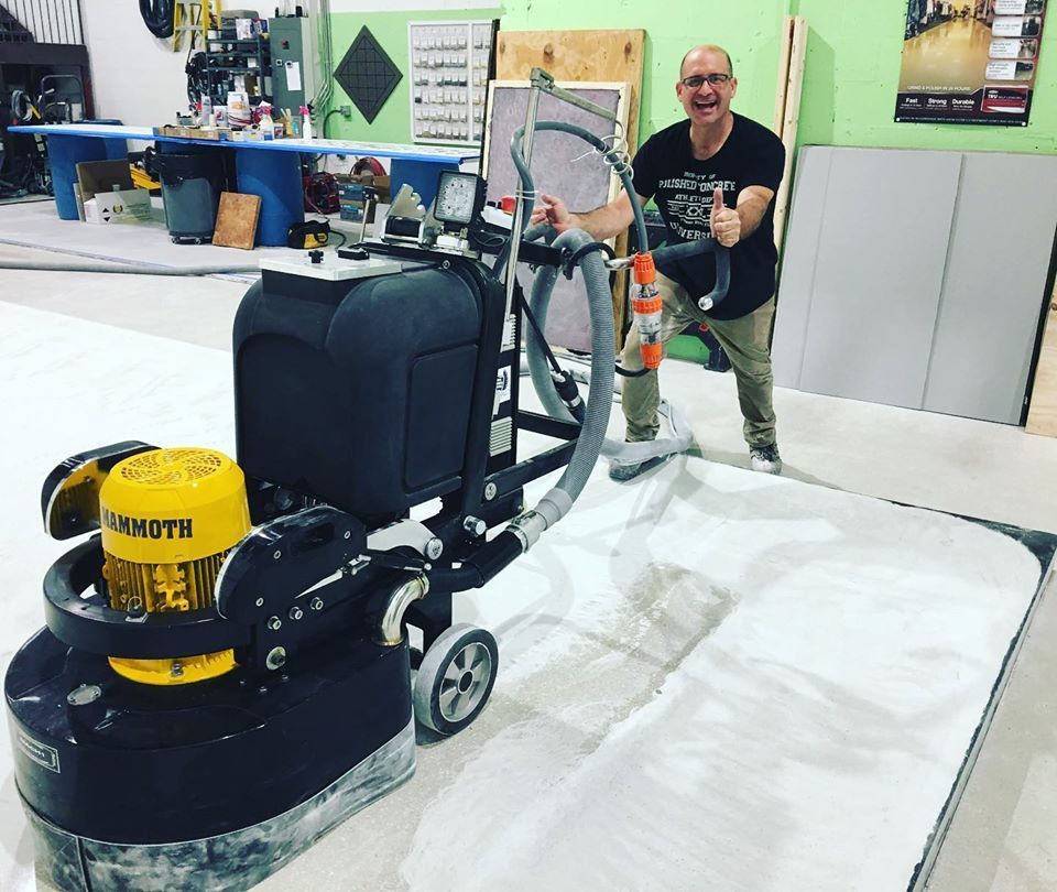 Man operating a large floor grinding machine in a workshop; thumbs up.