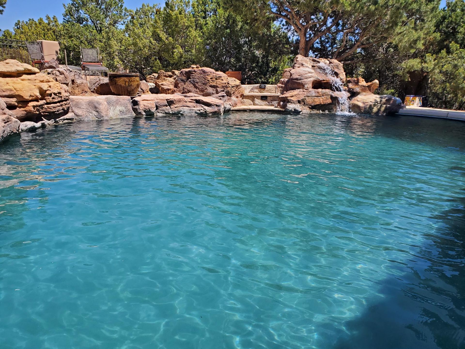 A Large Swimming Pool Surrounded by Rocks and Trees With a Waterfall in the Background