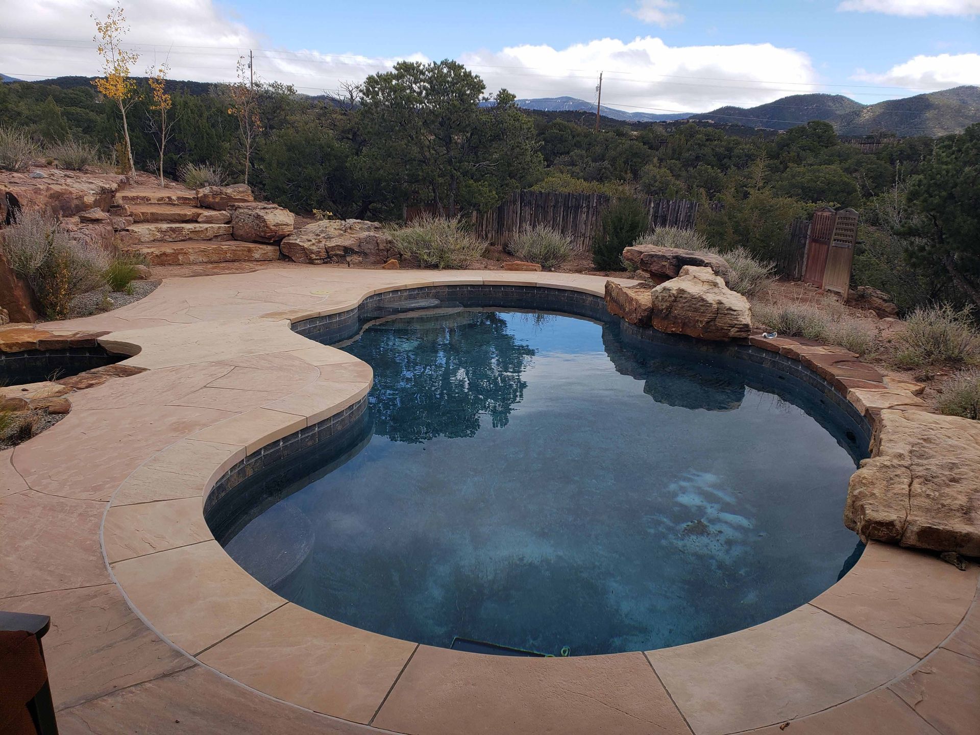 A large swimming pool surrounded by rocks and trees with mountains in the background