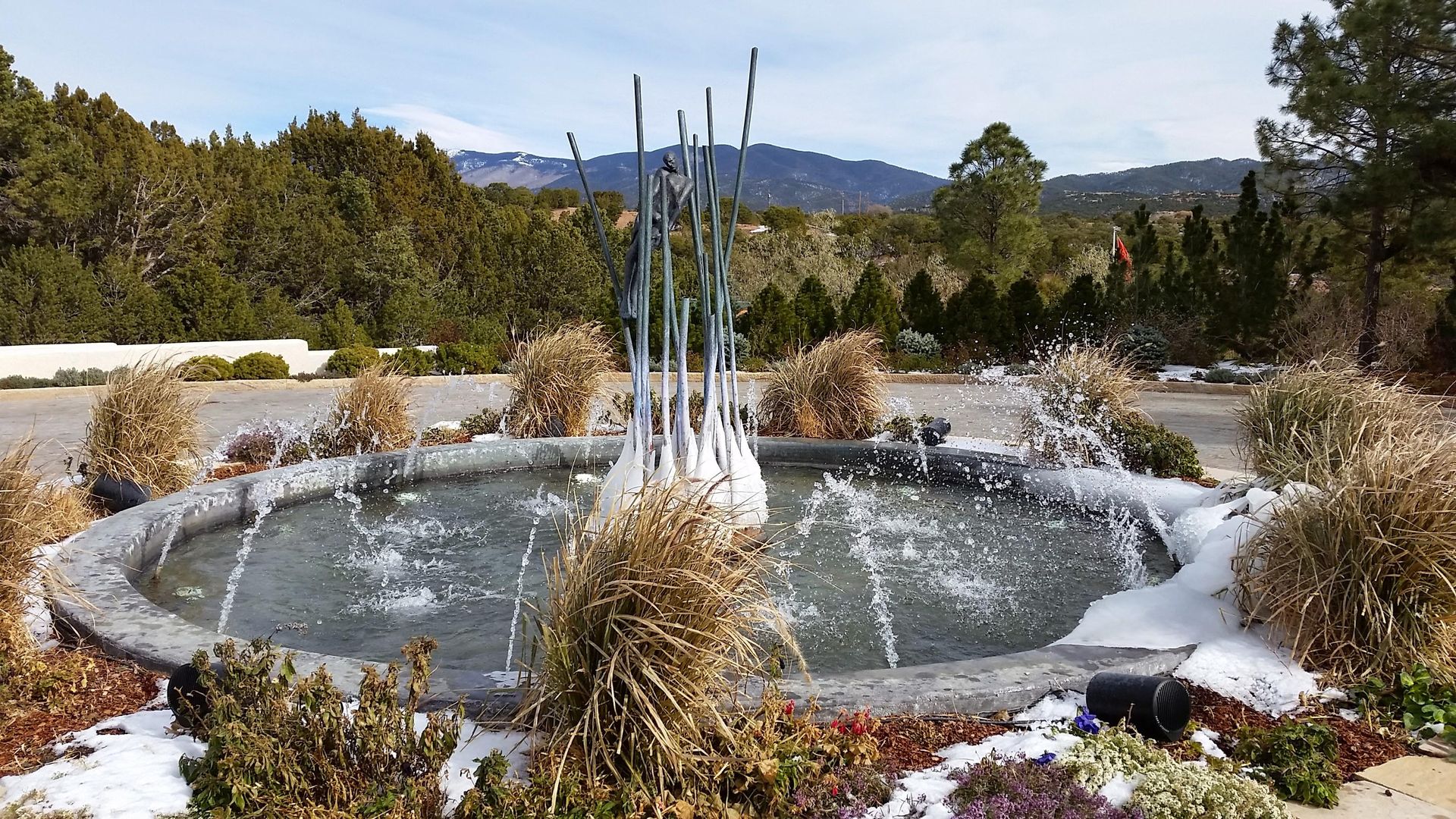 A fountain in the middle of a garden with mountains in the background