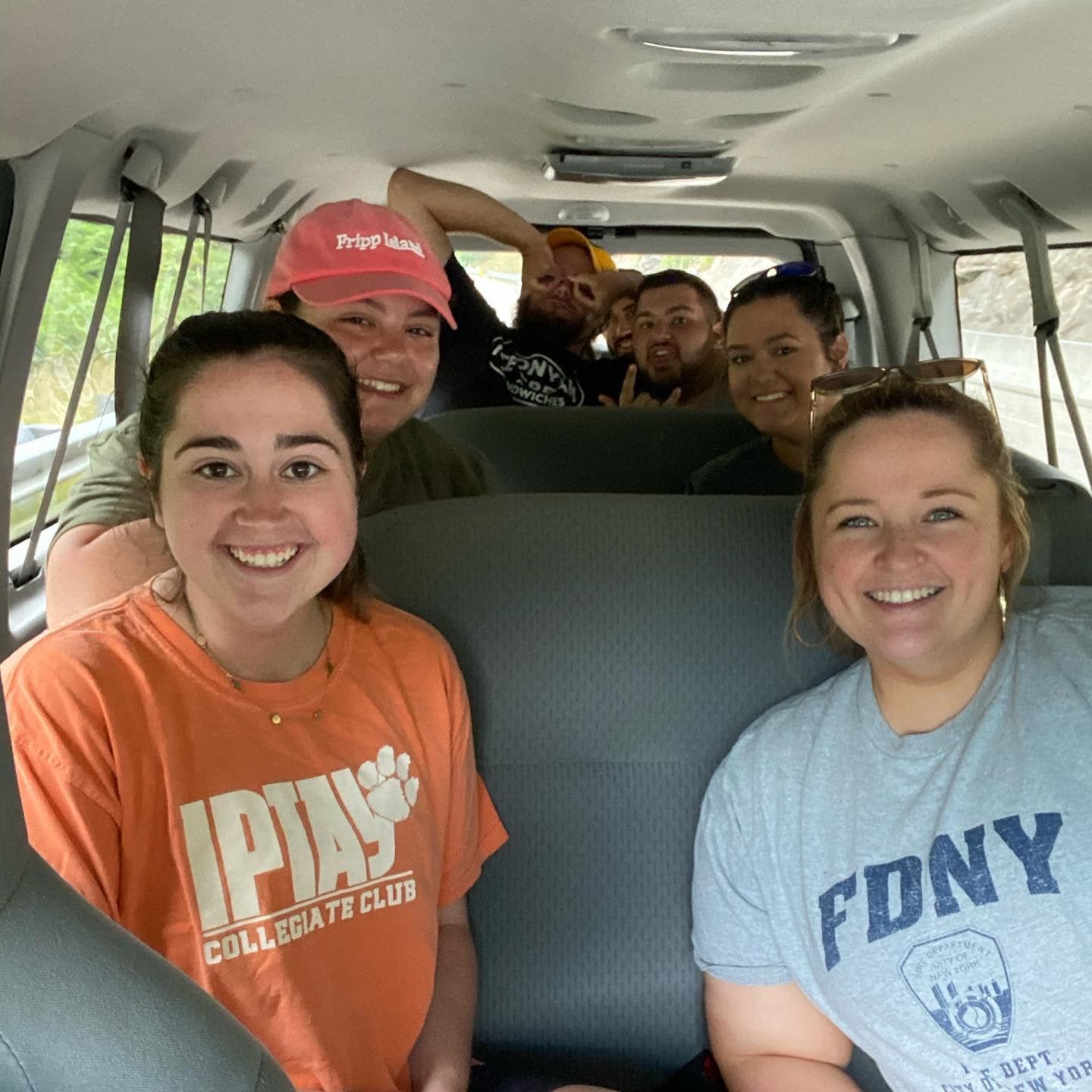 Group of smiling people inside a van. Two women in the foreground, several others behind them.