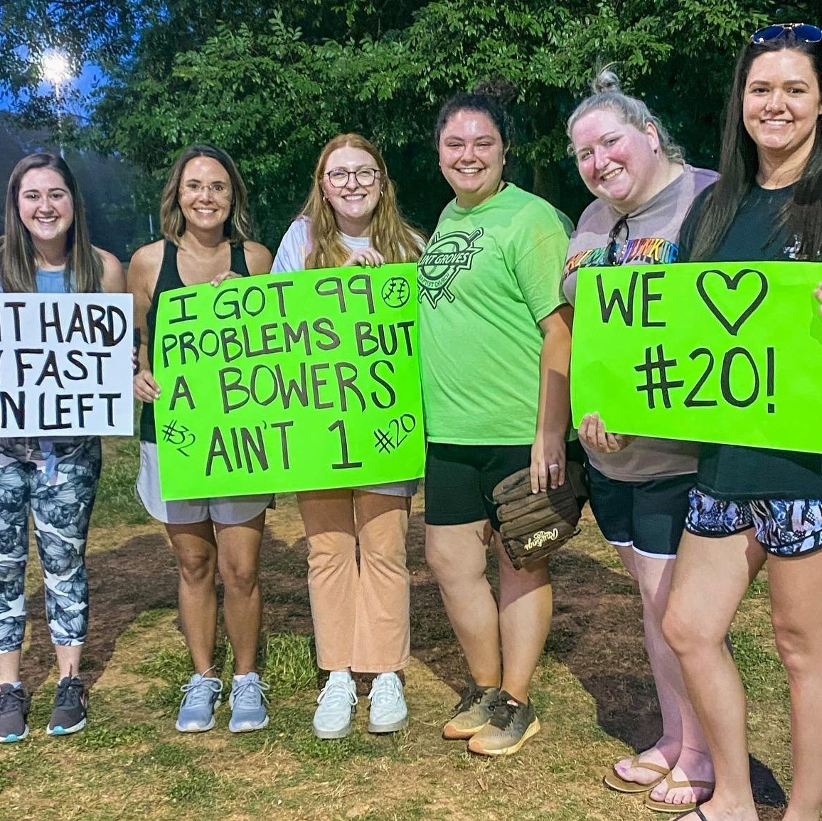 Six smiling women hold signs at an outdoor event. Signs read: 