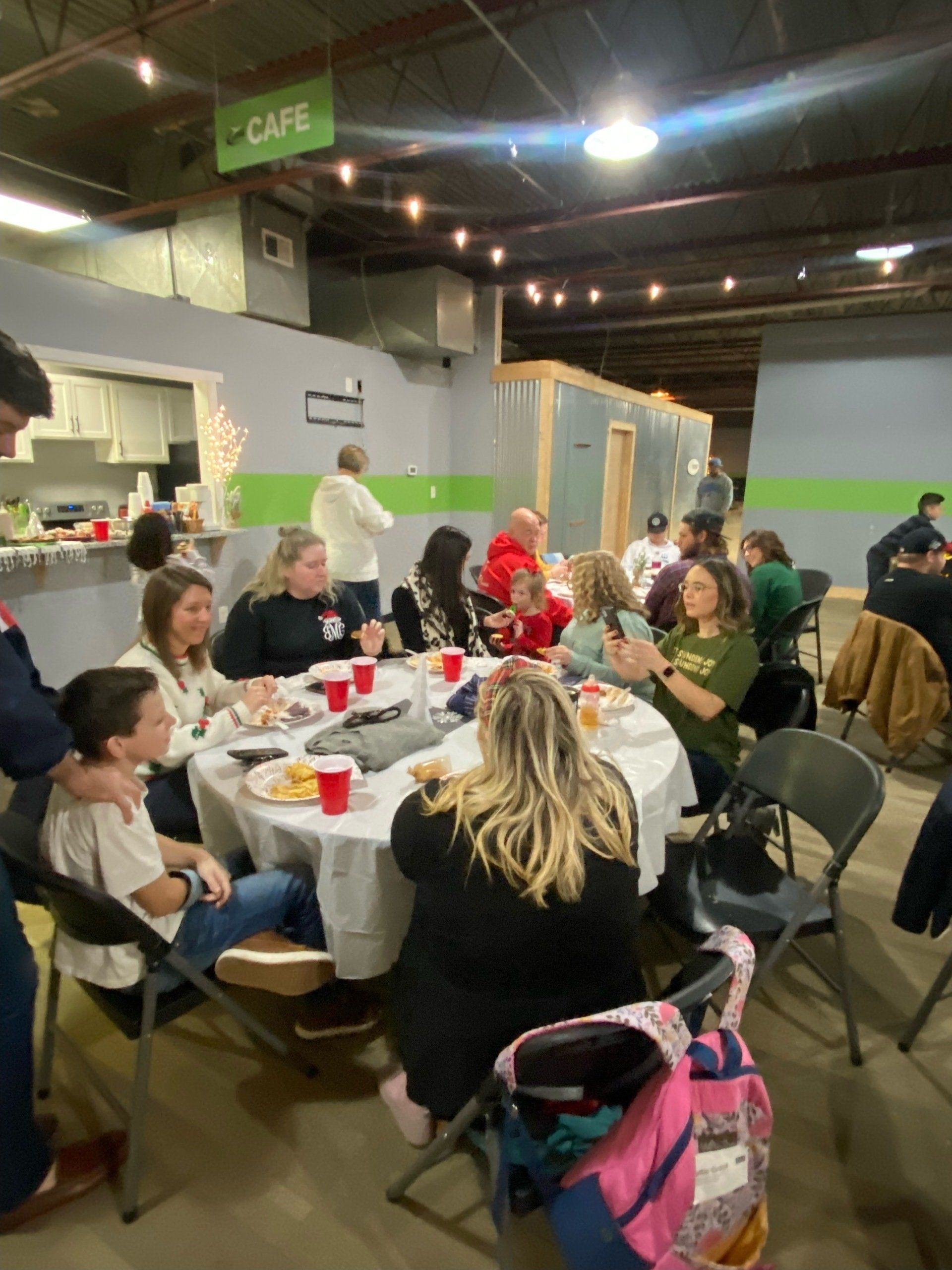 People gathered around a round table in a cafe, some smiling and eating. The room is decorated with string lights.