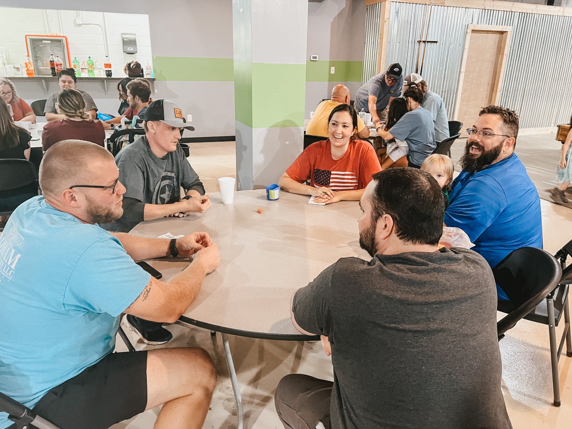 People gathered around tables in a community space. Some play games, while others work on projects, creating a collaborative atmosphere.