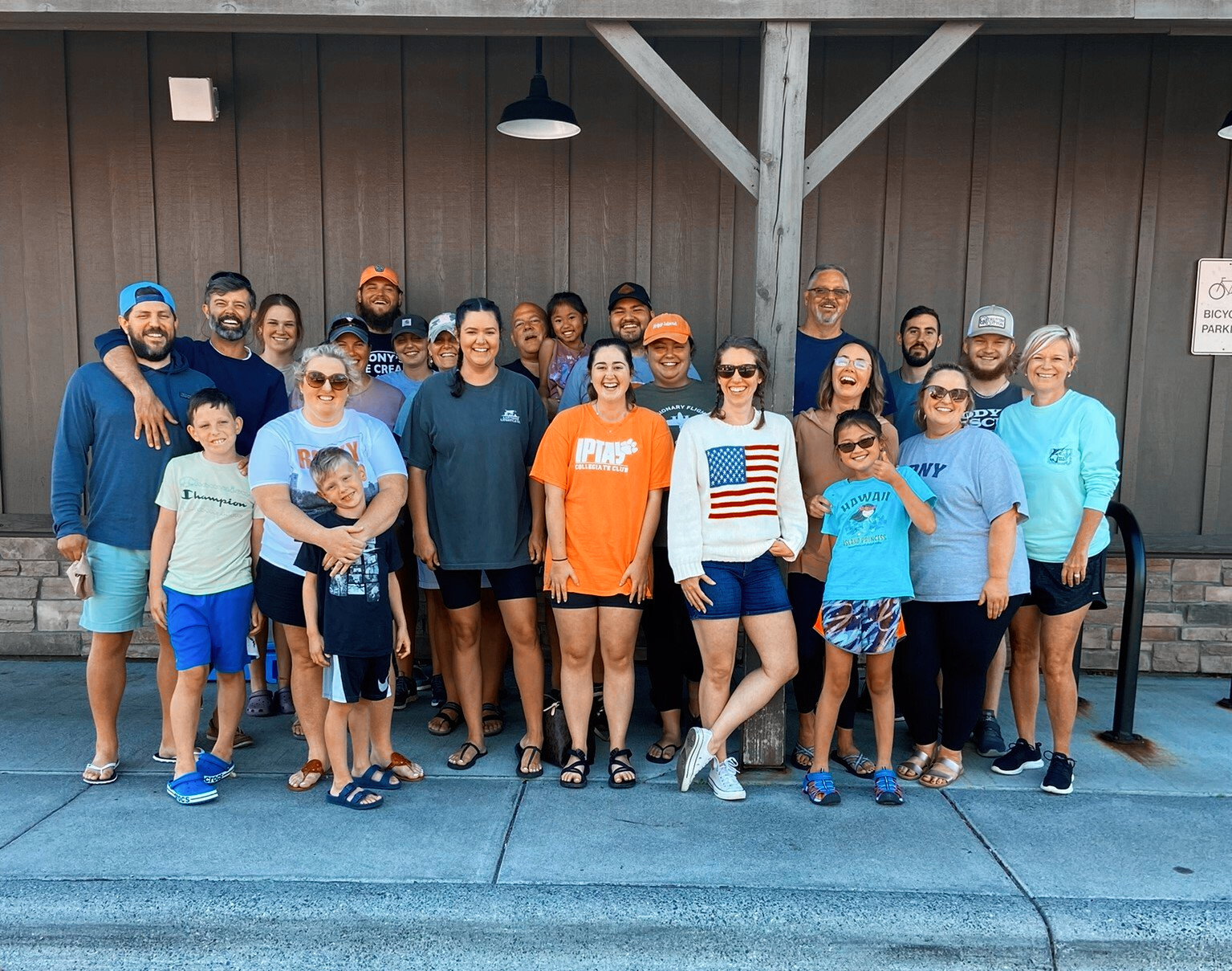 A large group of people standing outside a building. Many are smiling and wearing casual clothes, some with children.
