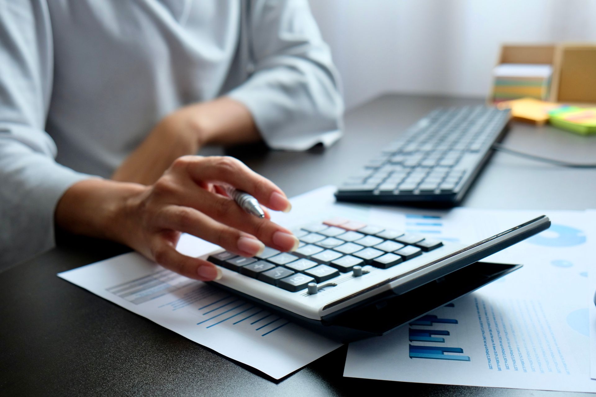 A person is typing on a calculator while sitting at a desk.