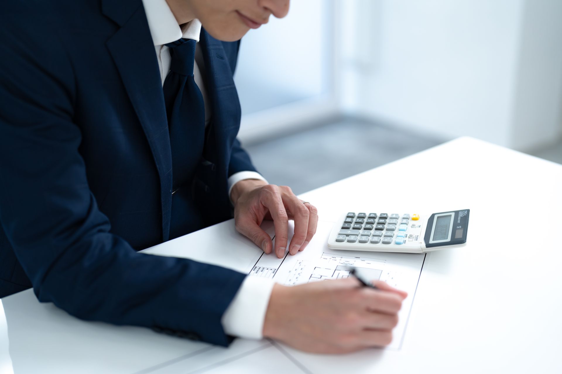 A man in a suit and tie is sitting at a desk using a calculator.