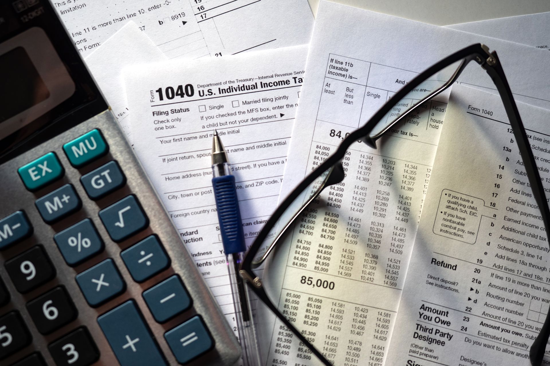 A 1040 tax form is next to a calculator and glasses