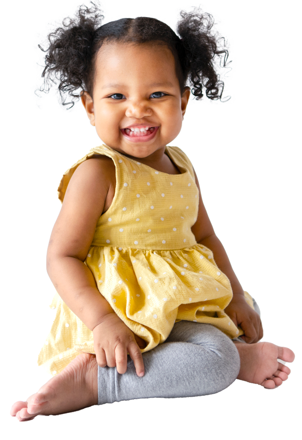A little girl in a yellow dress is sitting on the floor and smiling.