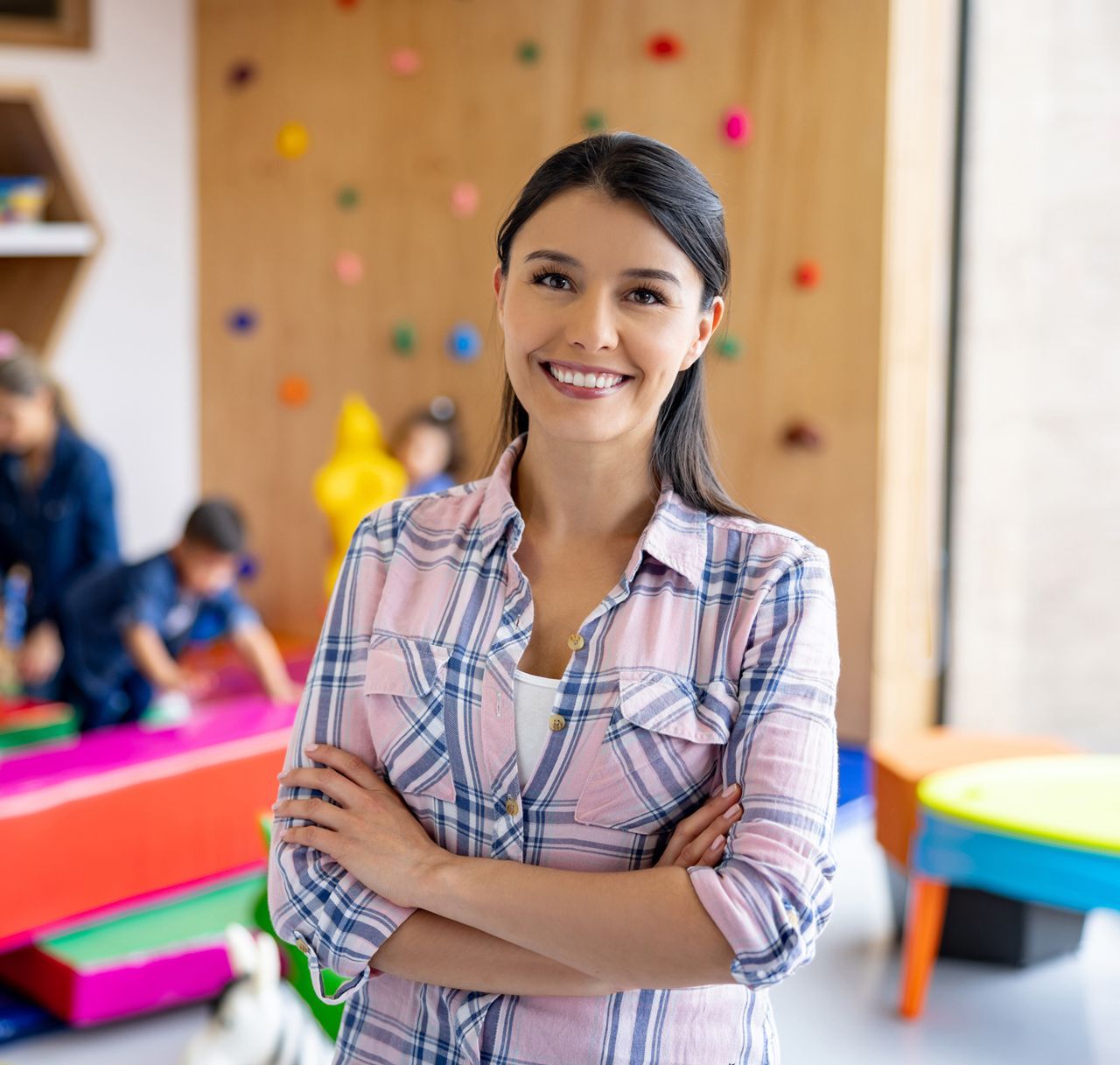 A woman is standing in a room with her arms crossed and smiling.