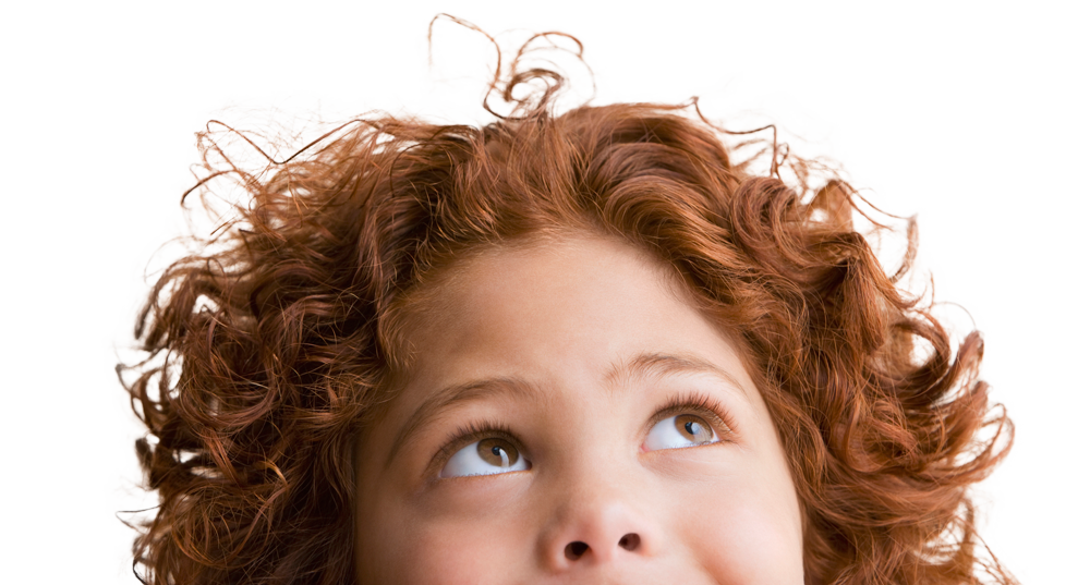 A young girl with curly red hair is looking up at the sky.