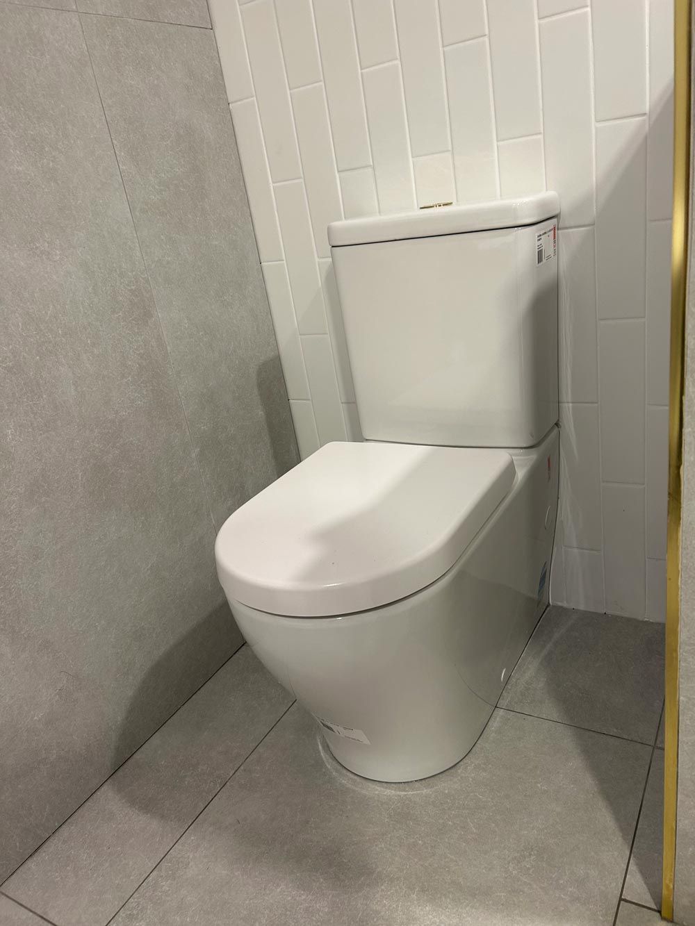 Clean Closed White Toilet Seat With Big Tiles On Floor — Professional Plumbing in Mittagong, NSW