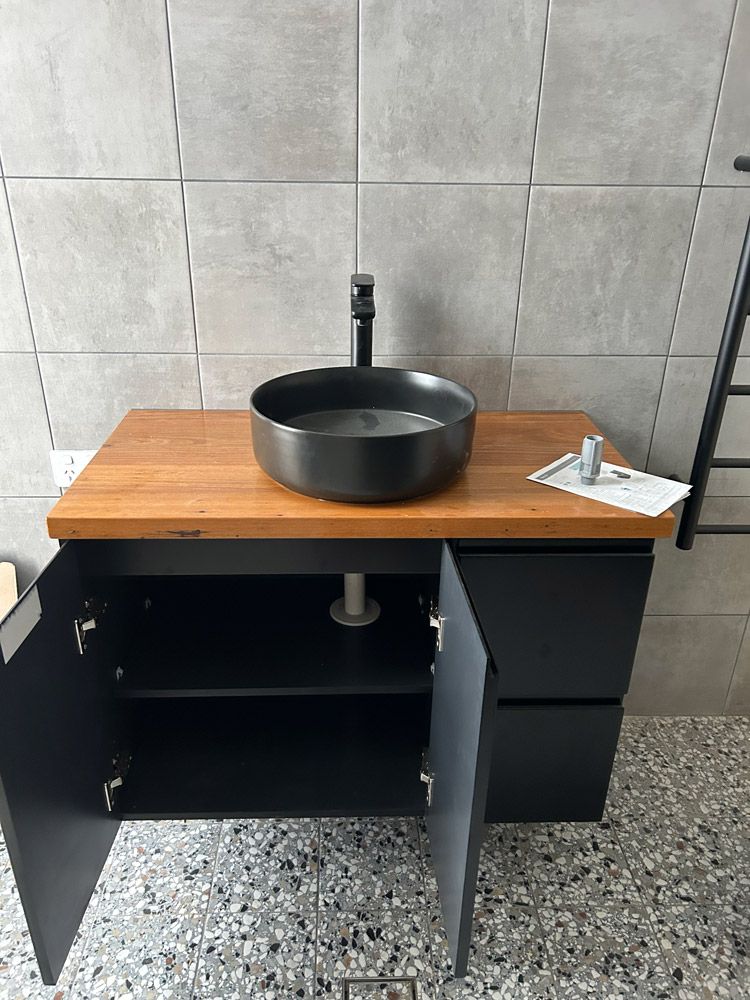 A Modern Bathroom With A Black Sink And Faucet On A Wooden Countertop, With Black Storage Cabinets A