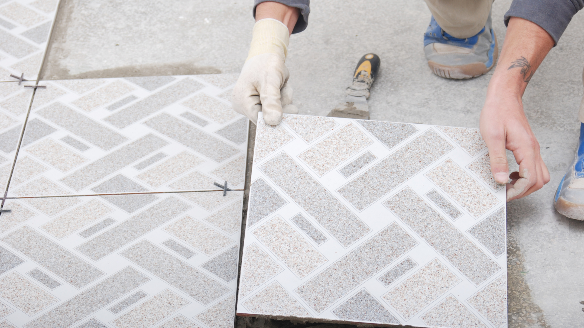 A person is laying tiles on a concrete floor.