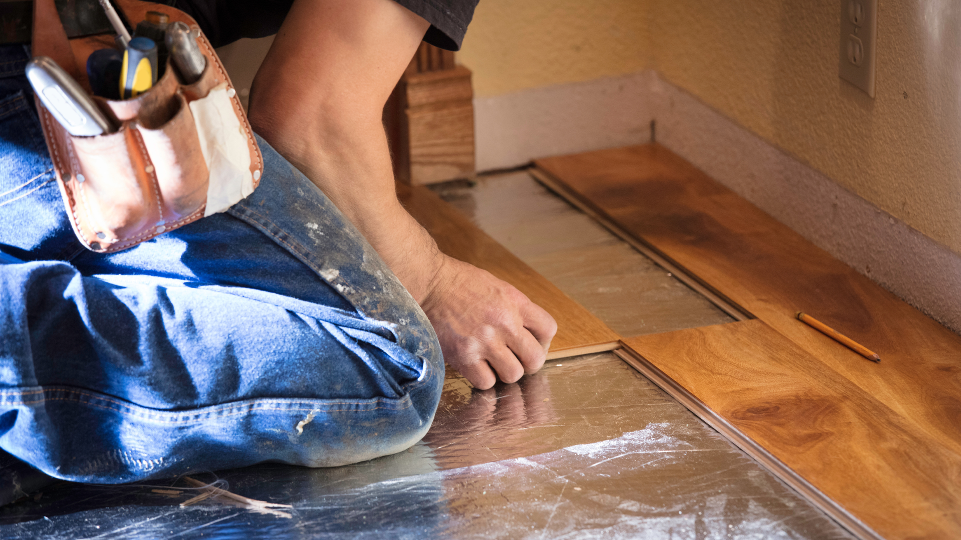 A man is kneeling down to install a wooden floor.