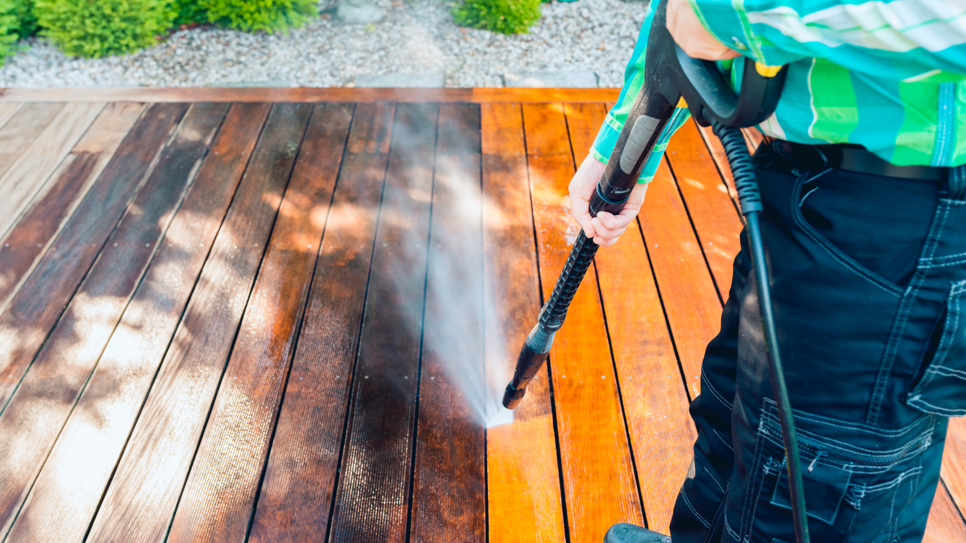 A person is cleaning a wooden deck with a high pressure washer.