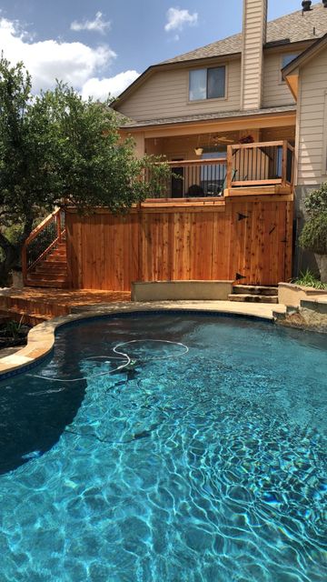 A large swimming pool in front of a house with a wooden deck.