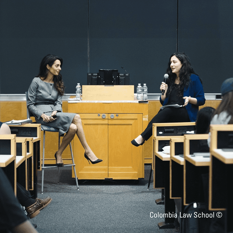 Natia Navruzov and Amal Clooney are sitting in front of a microphone at Columbia Law School