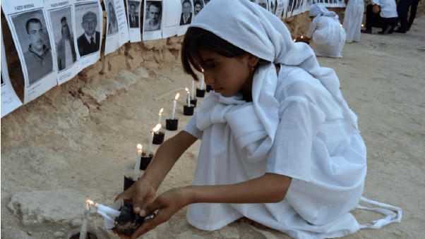 Yazidi girl wearing white and lighting candles in front of the photos of missing people