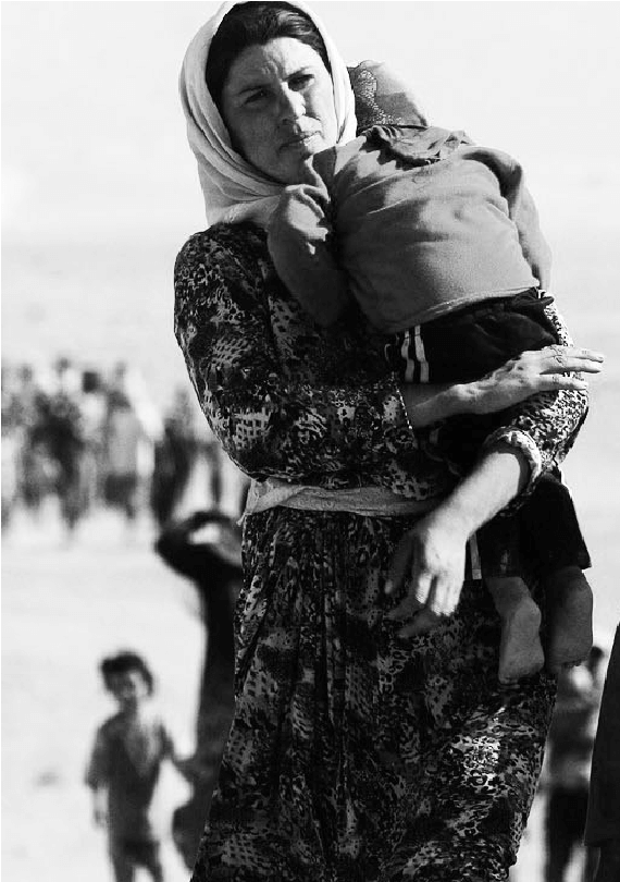 A Yazidi woman holding her child and walking in the desert fleeing Genocide